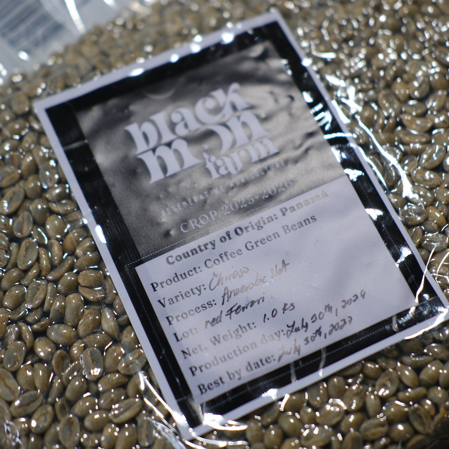 A close-up of a clear plastic bag filled with green coffee beans, featuring a black-and-white label from Black Muffin Farm with printed and handwritten details.