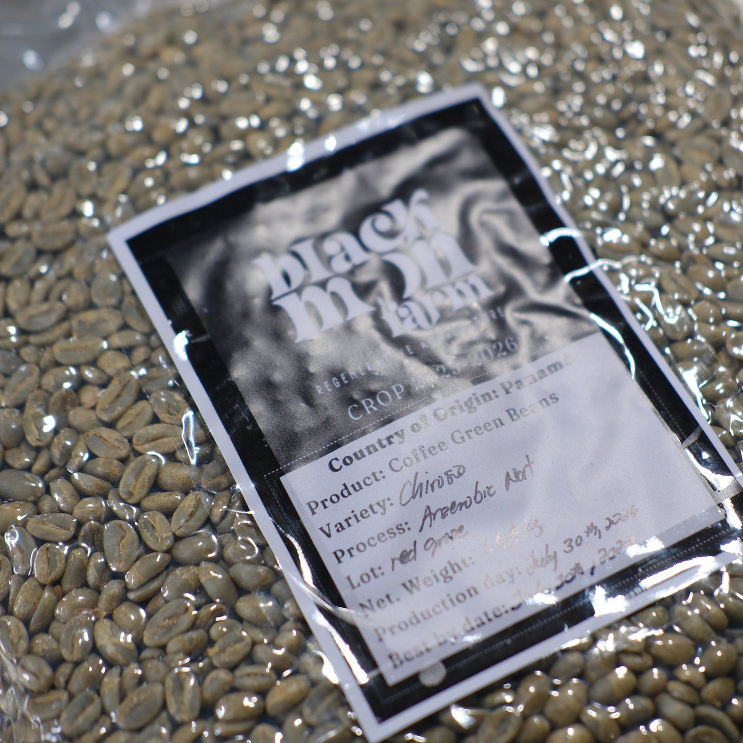 A close-up of coffee green beans inside a clear plastic bag with a printed label reading 'Black Marm Farm' and 'Café Green Beans,' showing the natural green-brown bean texture through the transparent packaging.